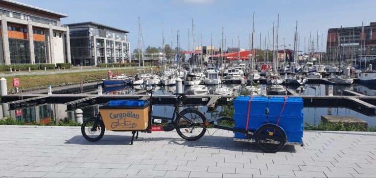 vélo cargo et sa remorque face au port de plaisance de Dunkerque. la remorque contient 12 caisses bleues de biodéchets